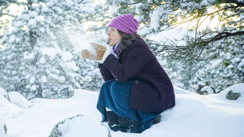 5 Tips to Overcome Winter Blues Image with Woman playing in snow.